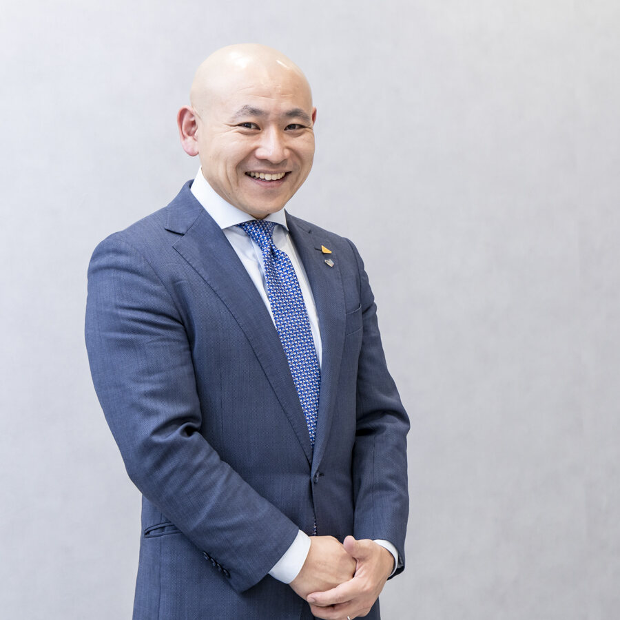 時 昴のポートレート。紺のスーツ、正面、笑顔